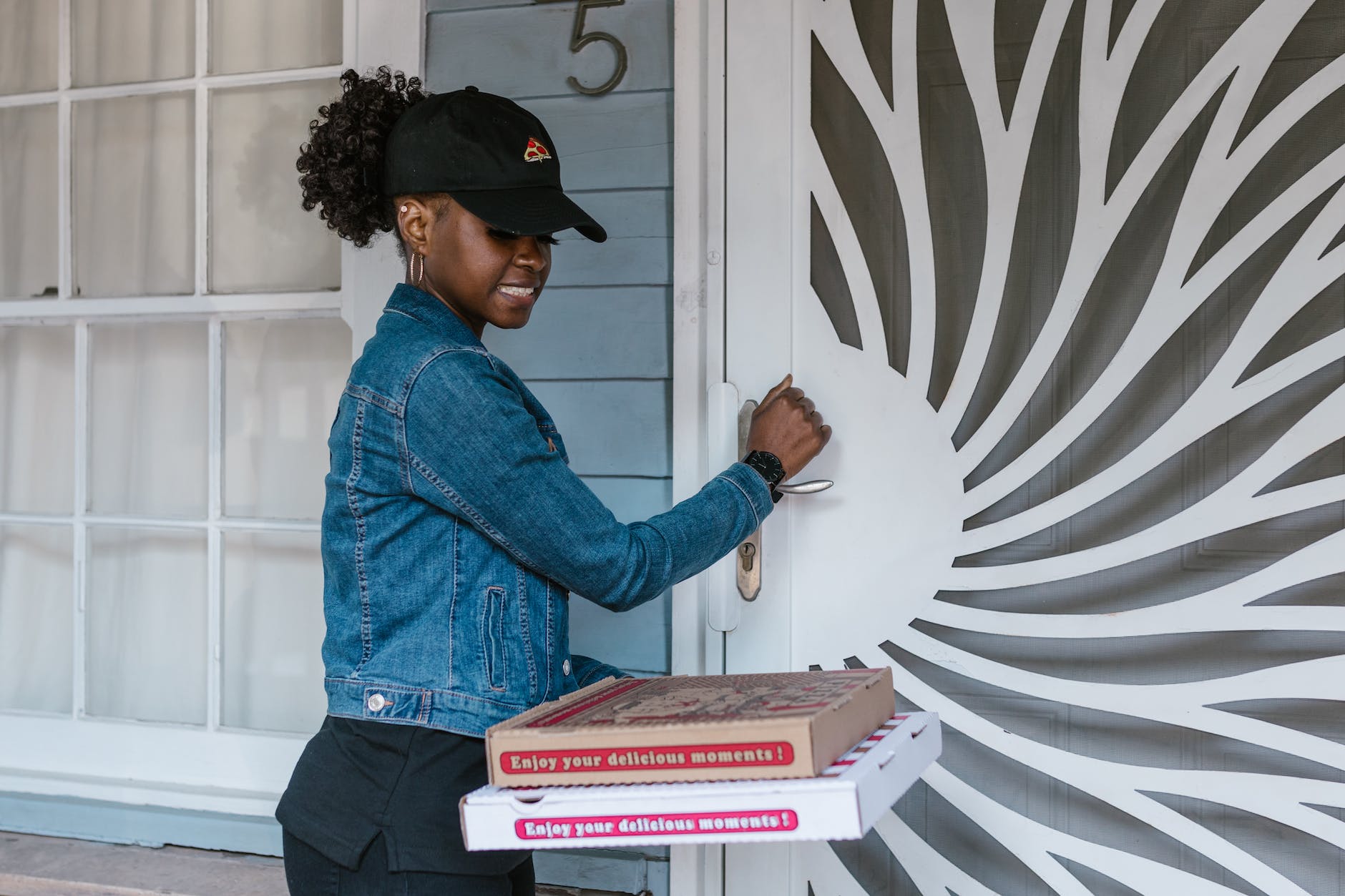 a woman in blue denim jacket holding pizza boxes