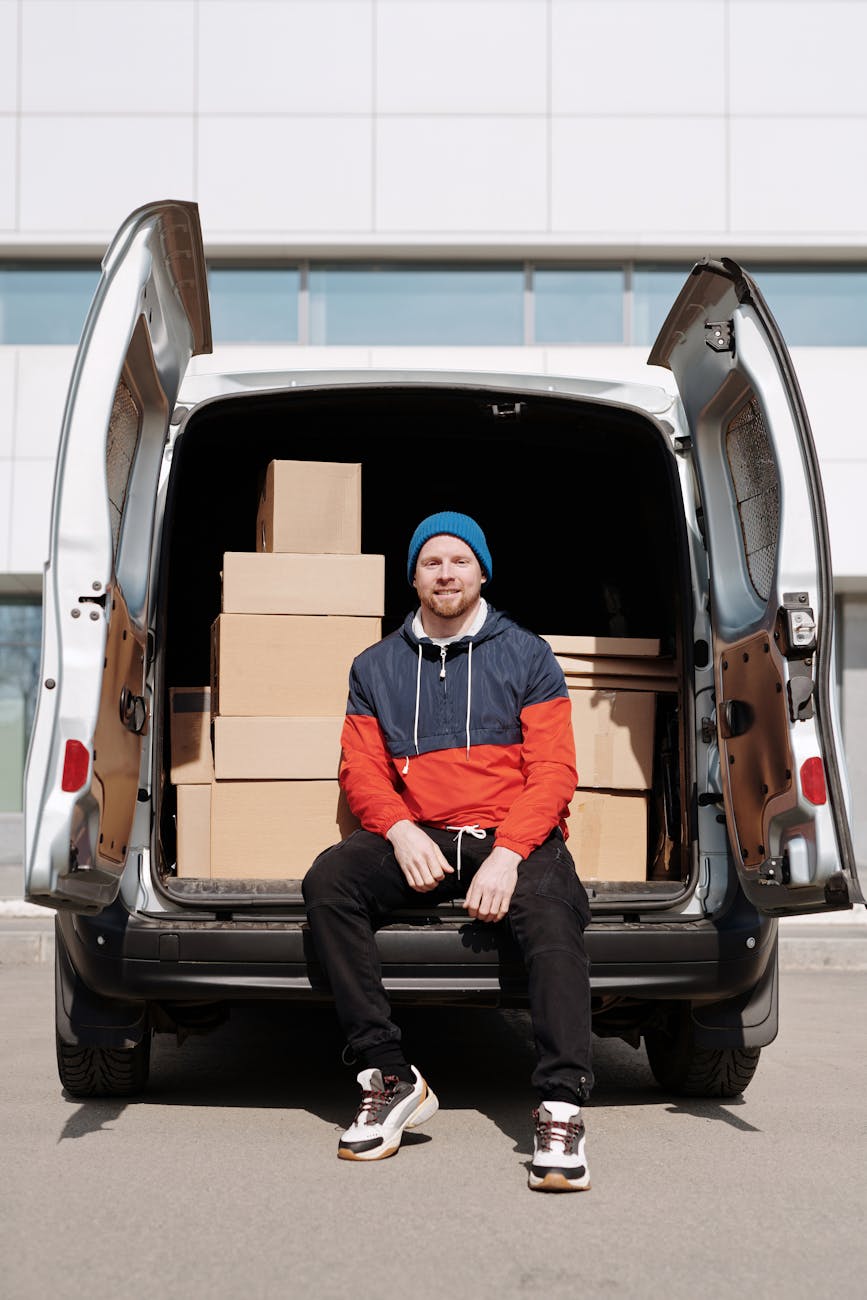 a man in a jacket sitting beside cardboard boxes